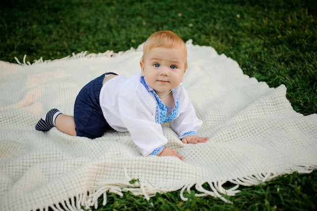 Kleine jongen gekleed in het geborduurde shirt liggend op de plaid op het groene gras