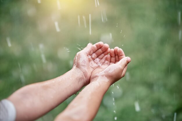 Kleine jongen geniet van warme zomerregen en vangt vallende druppels met palmen in de achtertuin van het huisje