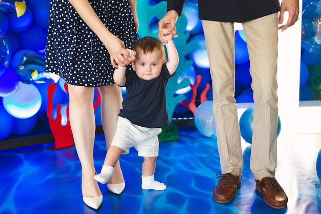 Kleine jongen houdt de hand van zijn vader en moeder vast en probeert de eerste stappen te zetten.