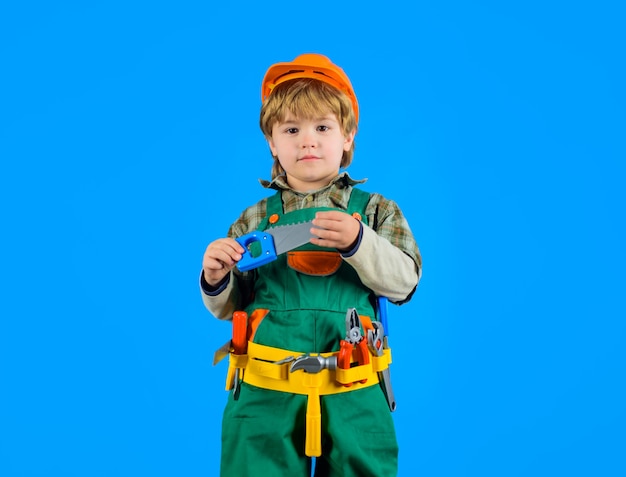 Kleine jongen in bouwersuniform houdt zaag vast, schattige jongen speelt bouwvakker kleine jongen met helm