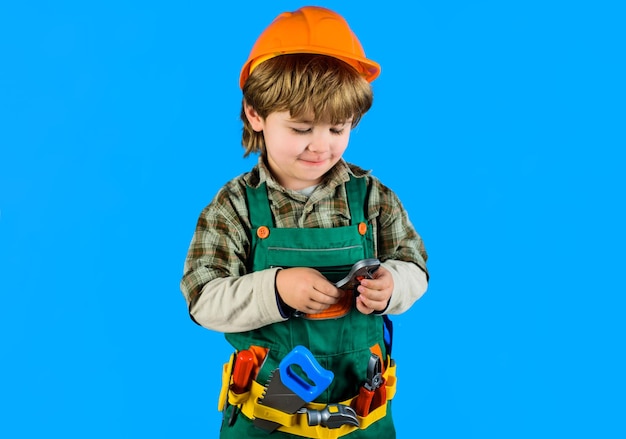 Kleine jongen in bouweruniform met moersleutel bouwer jongen in helm en gereedschap kinderspelgereedschap voor