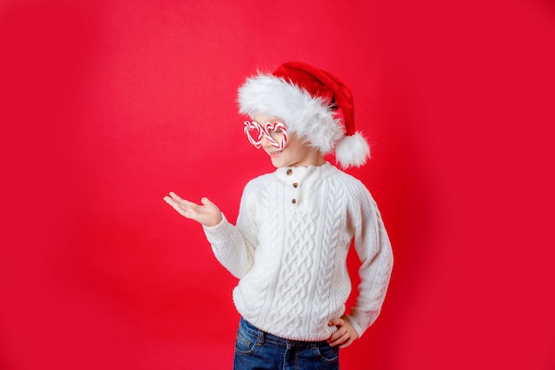 Kleine jongen in carnaval bril en kerstman hoed op rode achtergrond nieuwjaar