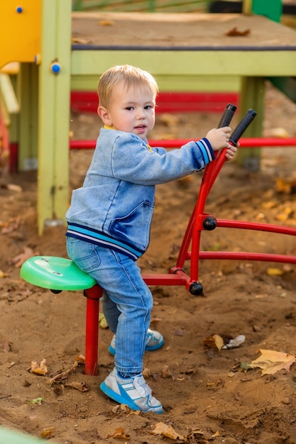 Kleine jongen in denim kleding speelt met een stuk speelgoed graafmachine op de speelplaats in het herfstpark.