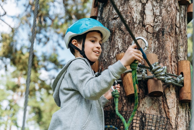 Kleine jongen in een beschermende helm haakt de karabijn aan het touw. Een kind in een touwpark