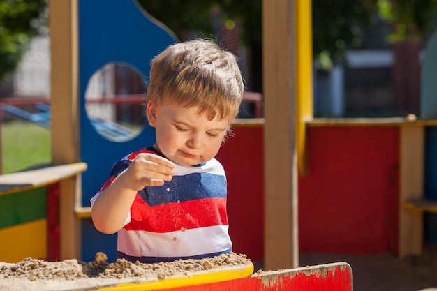 Kleine jongen in een gekleurd T-shirt speelt in de zandbak