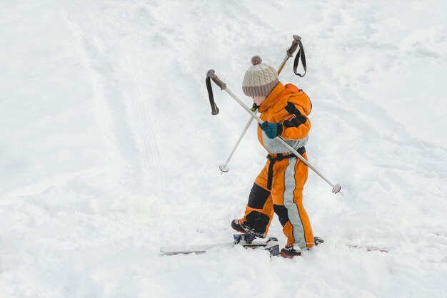 Kleine jongen in een oranje jumpsuit staat op ski's Winterdag Zijaanzicht