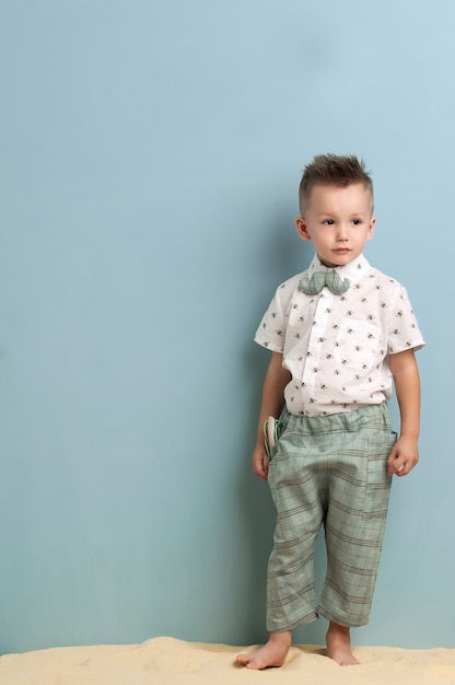 Kleine jongen in modieuze kleding en een katapult in zijn handen staat op het zand