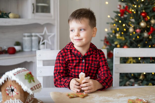 kleine jongen in rode pyjama met versierde kerstkoekjes voor peperkoekmannen