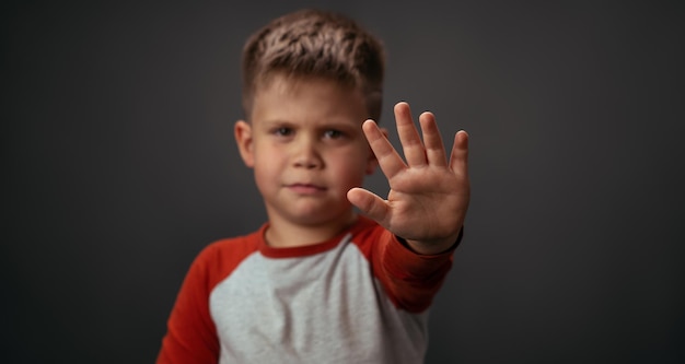 Kleine jongen in rood shirt ongelukkig weergegeven: stop met zijn hand geïsoleerd op grijze achtergrond menselijke emotie...