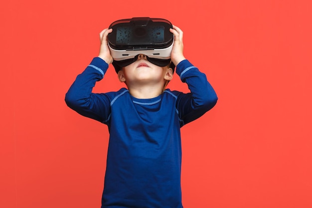 Kleine jongen in virtual reality-bril die het spel speelt op een rode achtergrond 3D-gadgettechnologie Kartonnen VR-headsetbril