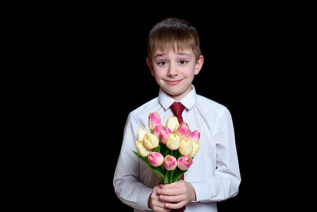 Kleine jongen in wit shirt geeft een boeket tulpen.