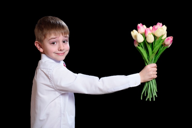 Kleine jongen in wit shirt geeft een boeket tulpen.