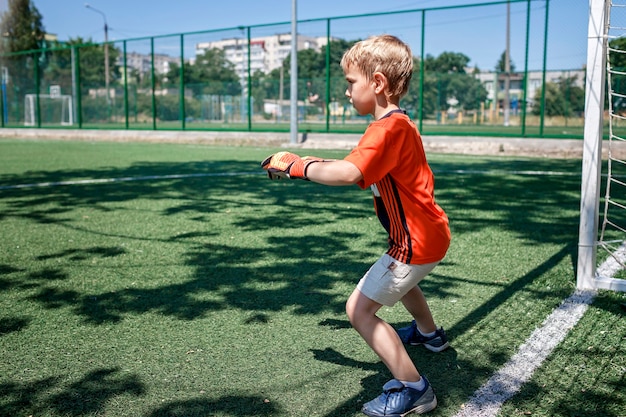 Kleine jongen in zwart en oranje voetbalvorm voetballen op open veld in de tuin jonge keeper