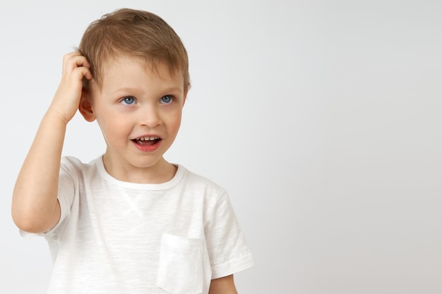 Kleine jongen is diep in gedachten en krabt zijn hoofd op een witte achtergrond