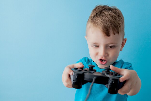 Kleine jongen jongen 2-3 jaar oud gekleed in blauwe kleren houden in de hand joystick voor gameson blauw kinderen studio portret. Mensen jeugd levensstijl concept. Bespreek kopie ruimte.