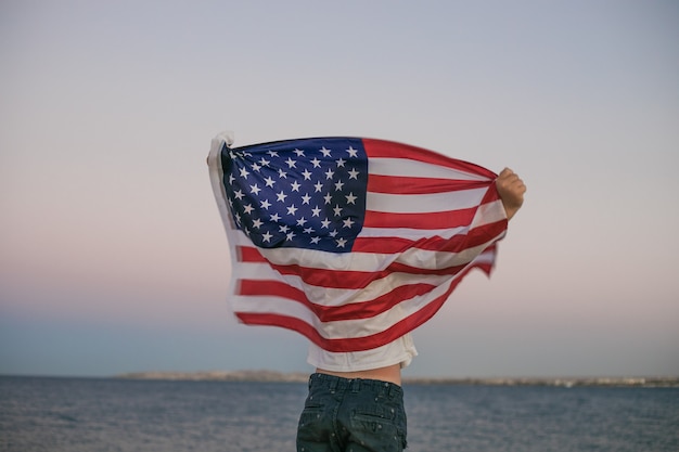 Kleine jongen laat de Amerikaanse vlag in zijn handen wapperen op de wind aan zee