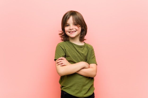 Kleine jongen lacht zelfverzekerd met gekruiste armen.