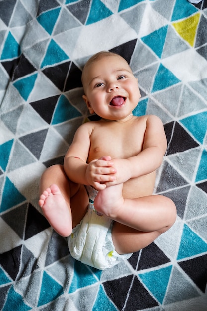 Kleine jongen leeftijd 8 maanden en lacht. Hij draagt een luier. Gezondheid en ontwikkeling van kinderen