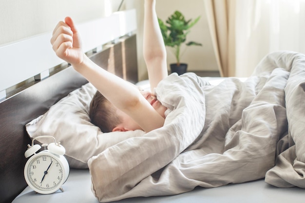 Kleine jongen liggend en strekkend in bed thuis in de ochtend met wekker