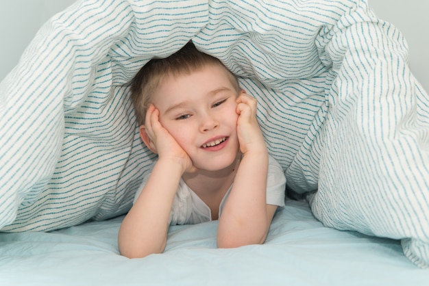 Kleine jongen ligt onder de deken en lachend