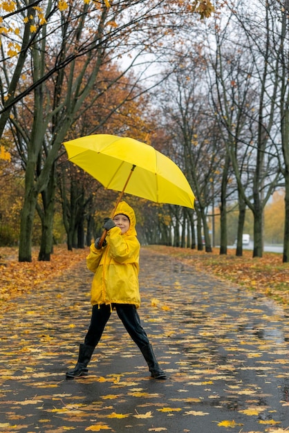 Kleine jongen loopt in het park en speelt met een gele paraplu Wandelen met kind in regen Verticaal frame