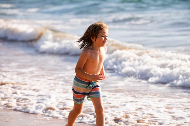 Kleine jongen loopt op de kust van het strand opspattend water in de blauwe zee, jongen die op het zomerstrand loopt