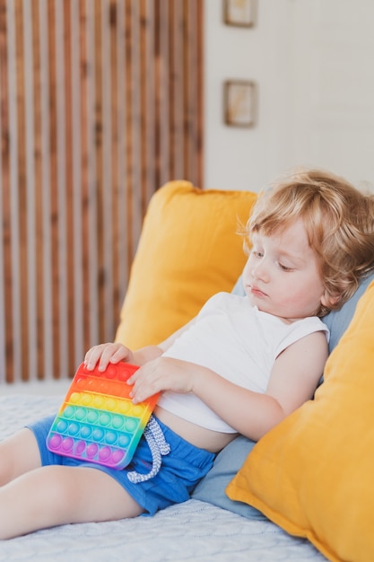 Kleine jongen met anti-stress zintuiglijk pop-it-speelgoed in zijn hand Jonge peuter speelt met zintuiglijk speeltje