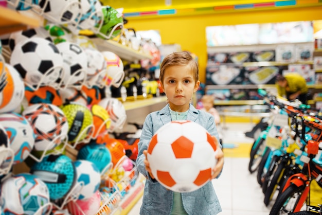 Kleine jongen met bal in kinderwinkel, vooraanzicht.