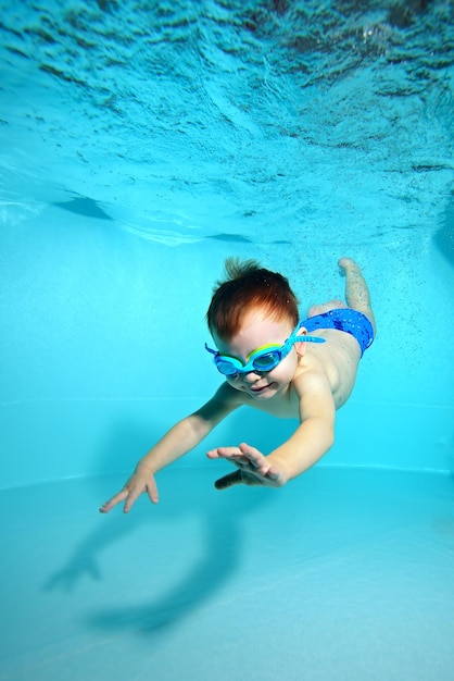 Kleine jongen met bril om te zwemmen duikt naar de bodem van het zwembad onder water