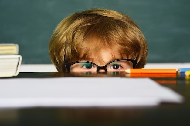 Kleine jongen met bril op zoek achter een bureau in de klas