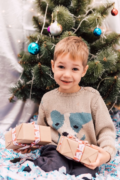 Kleine jongen met cadeautjes bij de kerstboom