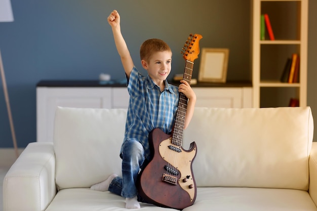 Kleine jongen met een gitaar op een bank thuis