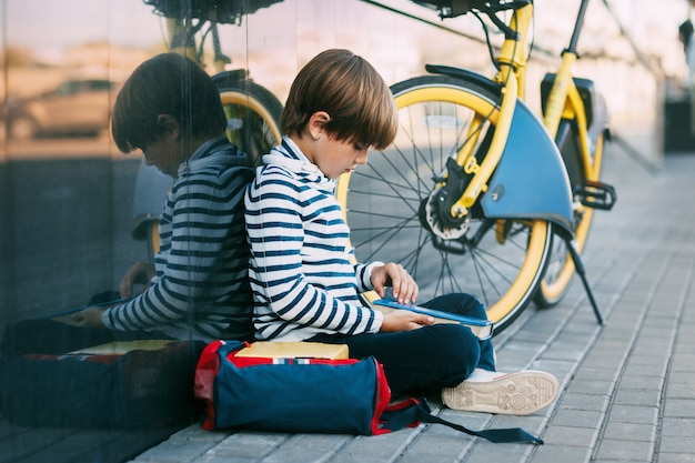 Kleine jongen met een rugzak lezen in de buurt van een fiets