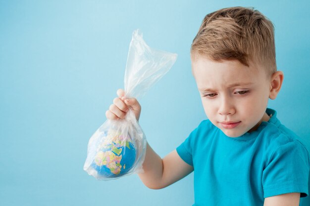 Kleine jongen met een wereldbol in een pakket op een blauwe achtergrond