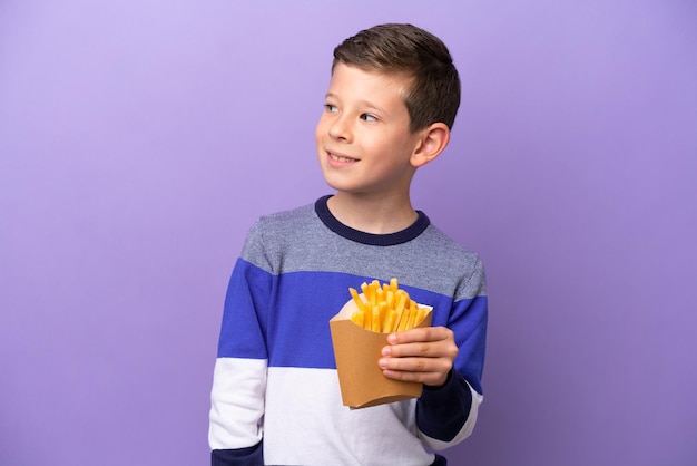 Kleine jongen met gebakken chips geïsoleerd op paarse achtergrond kijkend naar de zijkant en glimlachend