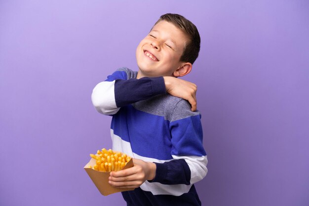 Kleine jongen met gefrituurde chips geïsoleerd op een paarse achtergrond die lijdt aan pijn in de schouder omdat hij zich heeft ingespannen