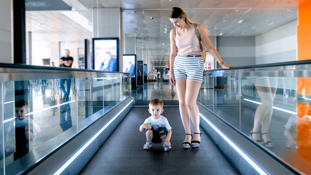 Kleine jongen met jonge moeder die op de horizontale roltrap staat in de luchthaventerminal.