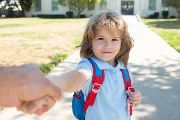 Kleine jongen met rugzak die de hand van de vader vasthoudt op de wazige achtergrond van het schoolgebouw kind met...