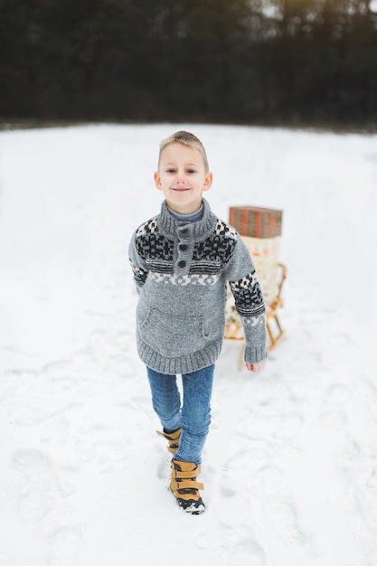 Kleine jongen met slee in besneeuwde bossen. Wintervakantie decoratie