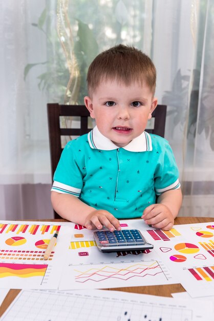 Kleine jongen met zakelijke grafieken en rekenmachine als analist