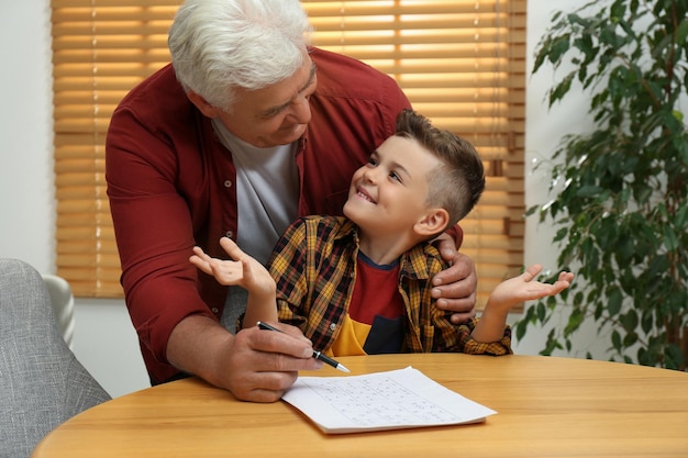 Kleine jongen met zijn grootvader sudoku puzzel oplossen aan tafel binnenshuis