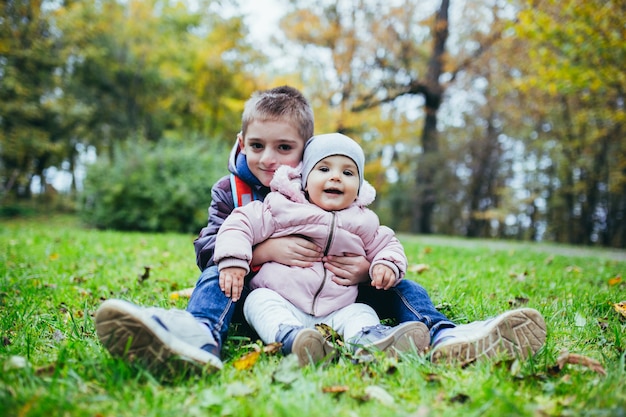 Kleine jongen met zijn zus in zijn armen, zittend op het gras