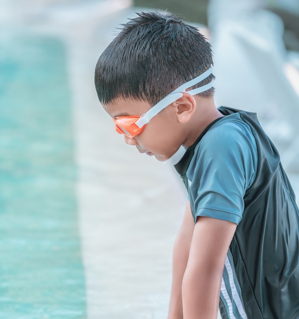 Kleine jongen met zwembril en zwemkleding speelt in het zwembad