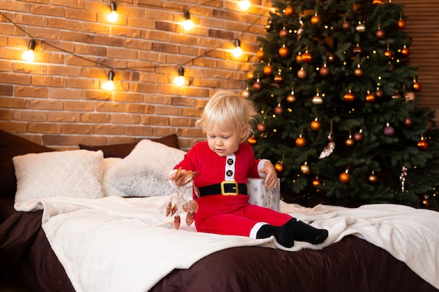 Kleine jongen op bed thuis in de buurt van de kerstboom. Nieuwjaar, winter en feestdagen seizoenen concept.