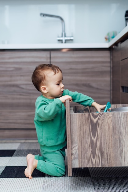 Kleine jongen opent de keukenlades om met keukengerei binnen te spelen Peuterjongen in gevaarlijke situatie thuis Veiligheidsconcept voor kinderen