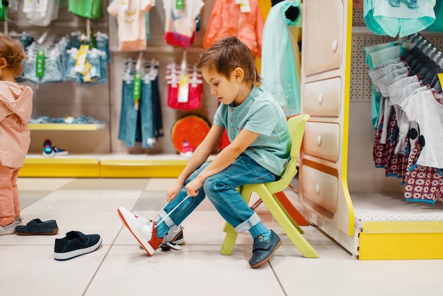 Kleine jongen probeert op schoenen in kinderwinkel, zijaanzicht. Zoon sneakers kiezen in de supermarkt, familie winkelen, jonge klant