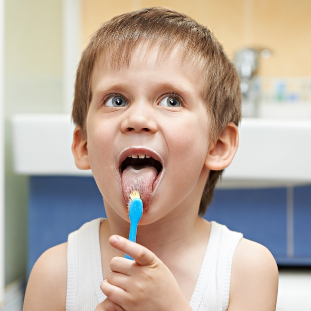 Kleine jongen reinigt de tong met een tandenborstel