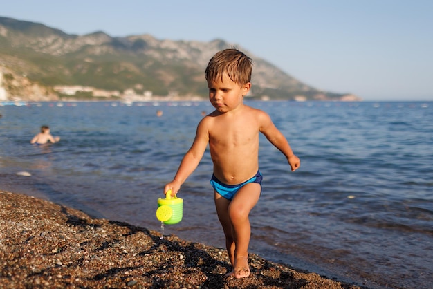 Kleine jongen rent langs de zandige kust met een speelgoedsproeier