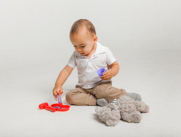 Kleine jongen speelt dokter en behandelt een knuffel met een stethoscoop. Kinderen en medicijnen, gezondheidszorg. studiofoto van hoge kwaliteit