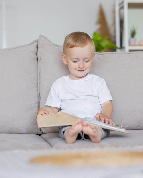 Kleine jongen speelt en leest een boek thuis op de bank in de woonkamer een europees kind